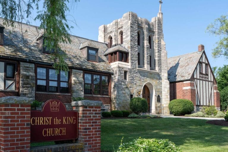 Historic stone facade of Christ the King Church surrounded by green lawns under a clear blue sky.