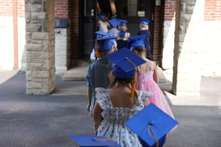 Children in blue caps walk in line during a kindergarten graduation ceremony.
