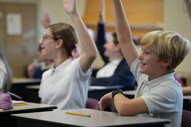 Students eagerly raise hands in a classroom, engaging in learning activities.