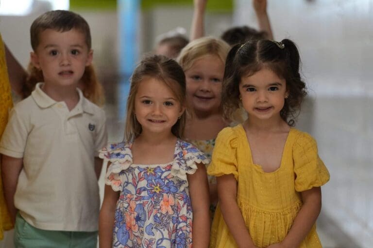 Group of smiling children in colorful outfits at a daycare center hallway.