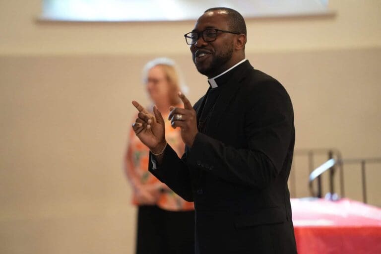 Clergy member speaking during church gathering, engaging audience with gesture. Focus keyword: church gathering.
