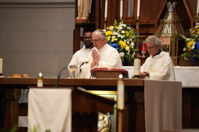 Priests conducting a church mass with flowers on the altar.