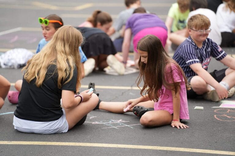 Children draw with sidewalk chalk at a community event, creating colorful street art.