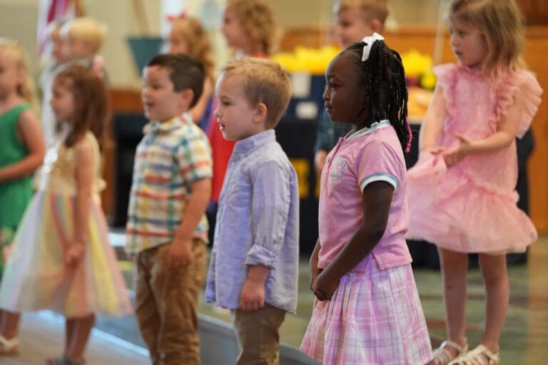 Children performing on stage during a preschool event, highlighting diversity and joy in learning.