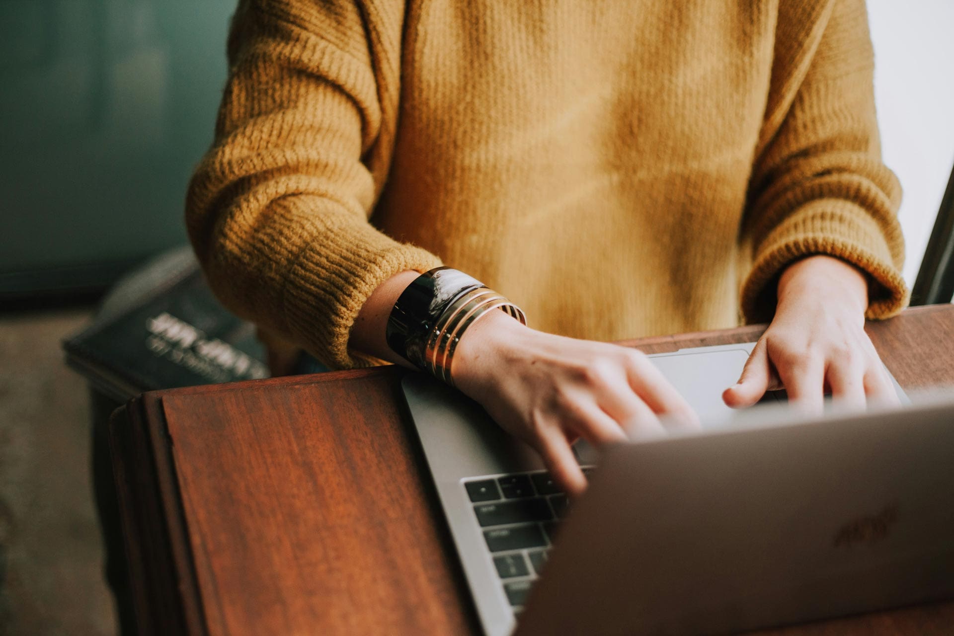 Person typing on laptop while wearing a mustard sweater, representing productivity in remote work.